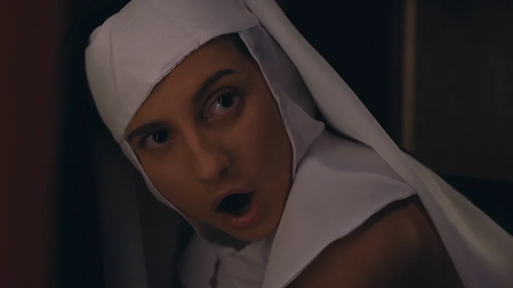 Close-up of a woman in a nun’s habit looking upward with her mouth open in a surprised expression.
