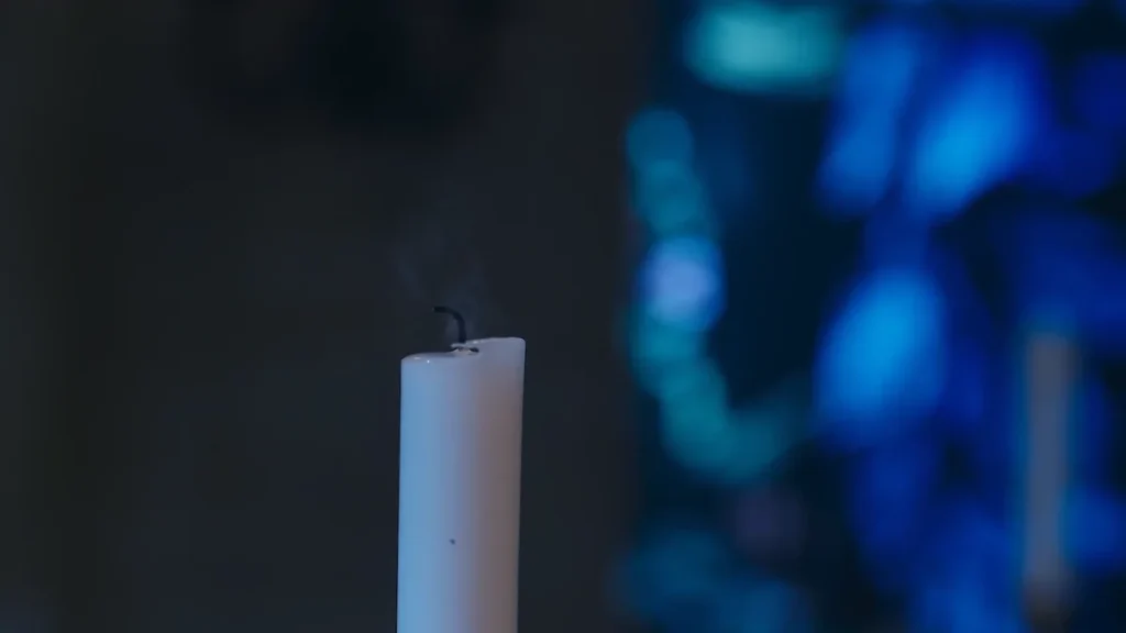 Close-up of a white candle with a extinguished wick and rising smoke against a dark background with blue bokeh lights.